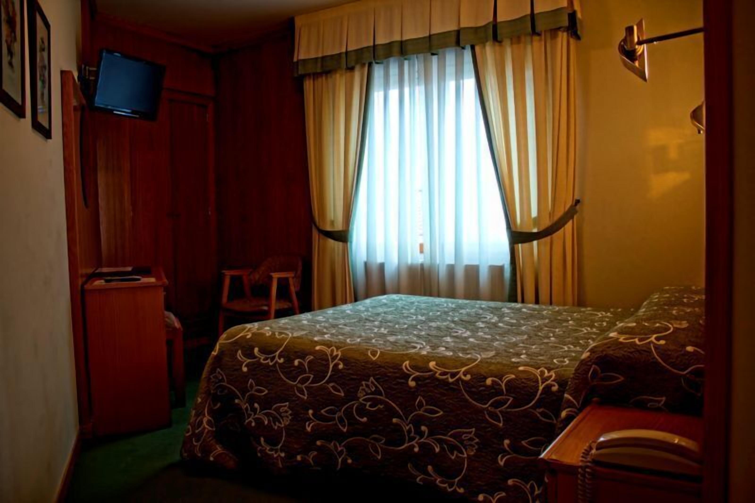 Een kamer met een bed, een bureau, een stoel en een aan de muur bevestigde televisie.