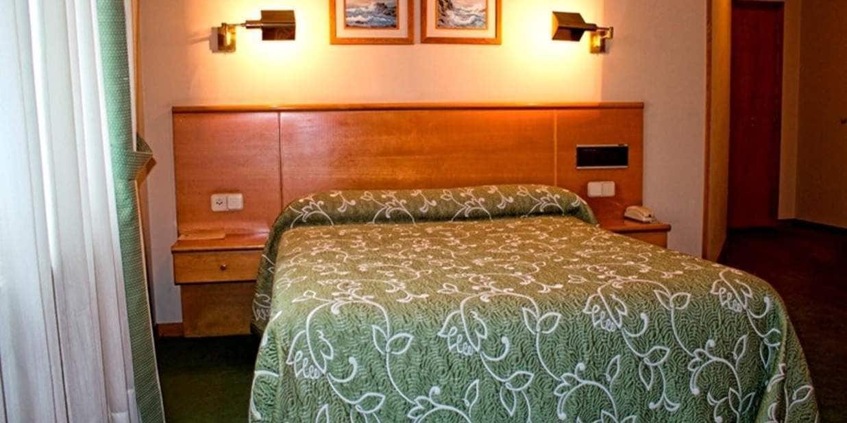 A hotel room with a bed, a nightstand, a lamp, and a wall-mounted telephone.