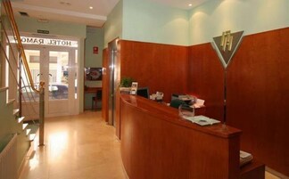 A hotel reception area with a wooden reception desk, a sign above the door, and a staircase to the left.