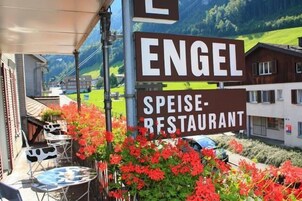Un letrero de restaurante con el nombre 'ENGEL SPEISE-RESTAURANT' y una vista de un pueblo con casas y vegetación al fondo.