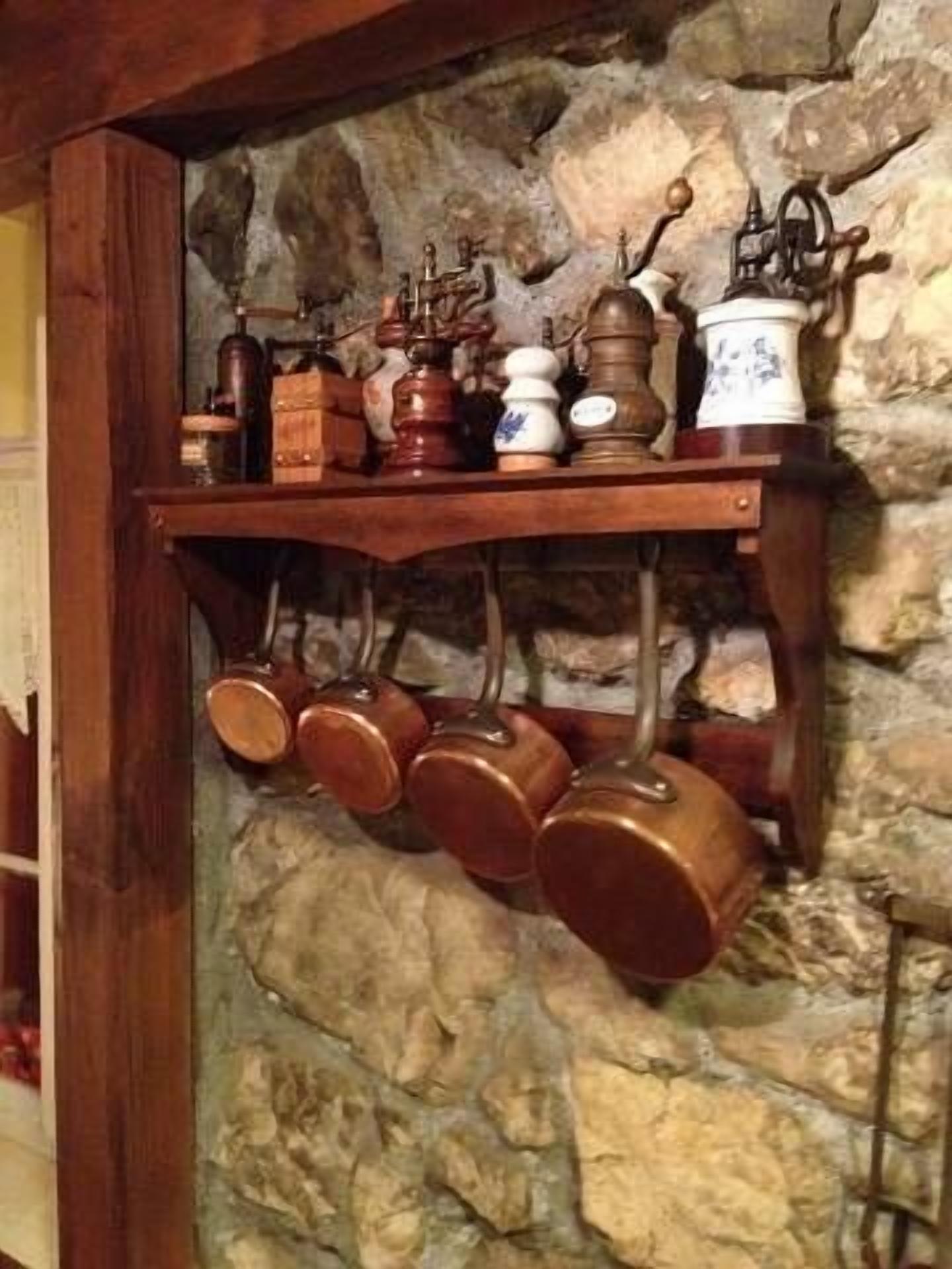 A wooden shelf with various kitchen utensils and a stone wall background.