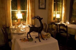 Comedor con mesas dispuestas para una comida, una figura decorativa de un ciervo en una de ellas, y una ventana con cortinas al fondo.