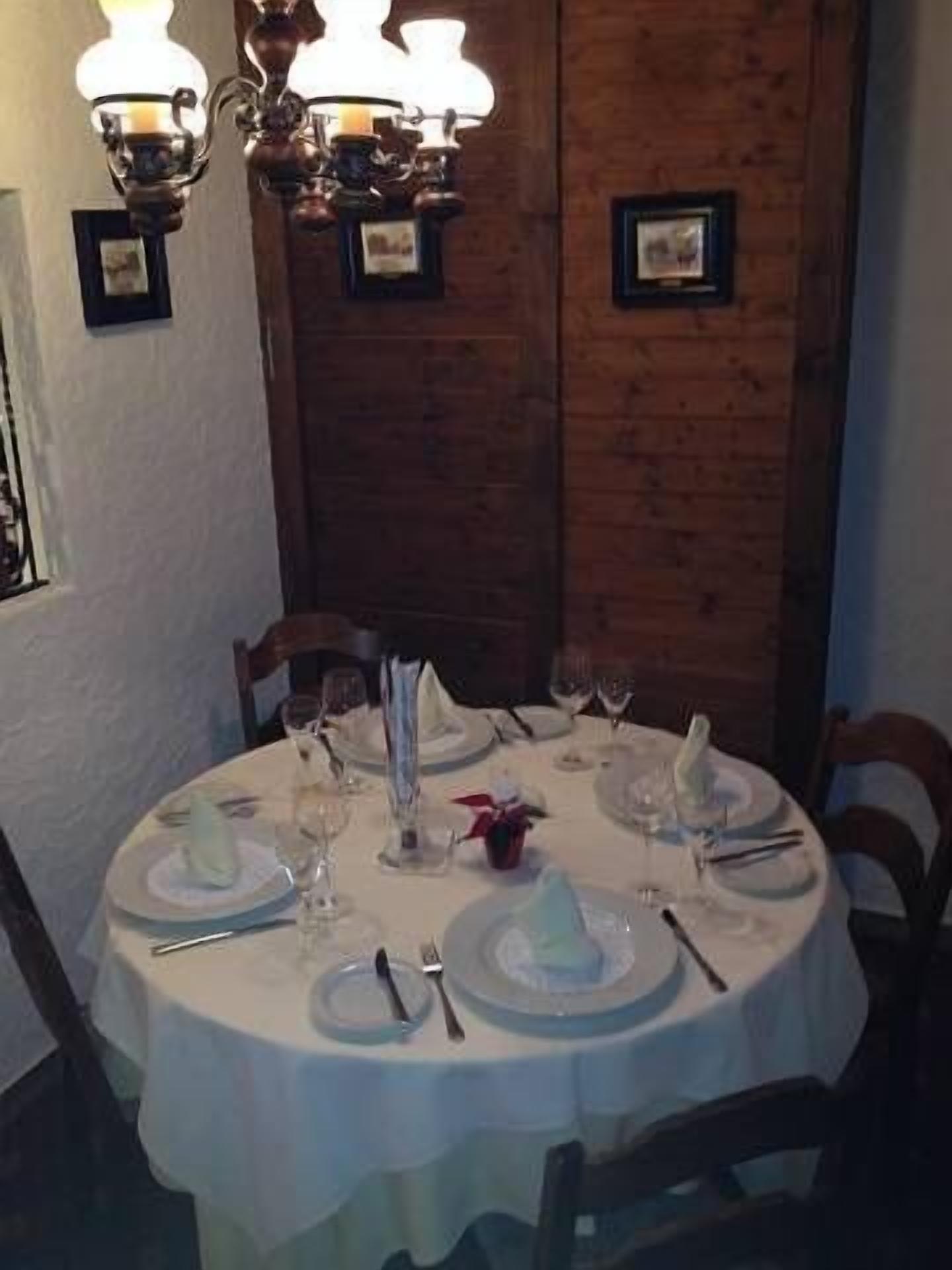 A round dining table set for four with white tablecloths, plates, cutlery, and glasses. There are two wall-mounted light fixtures above the table.