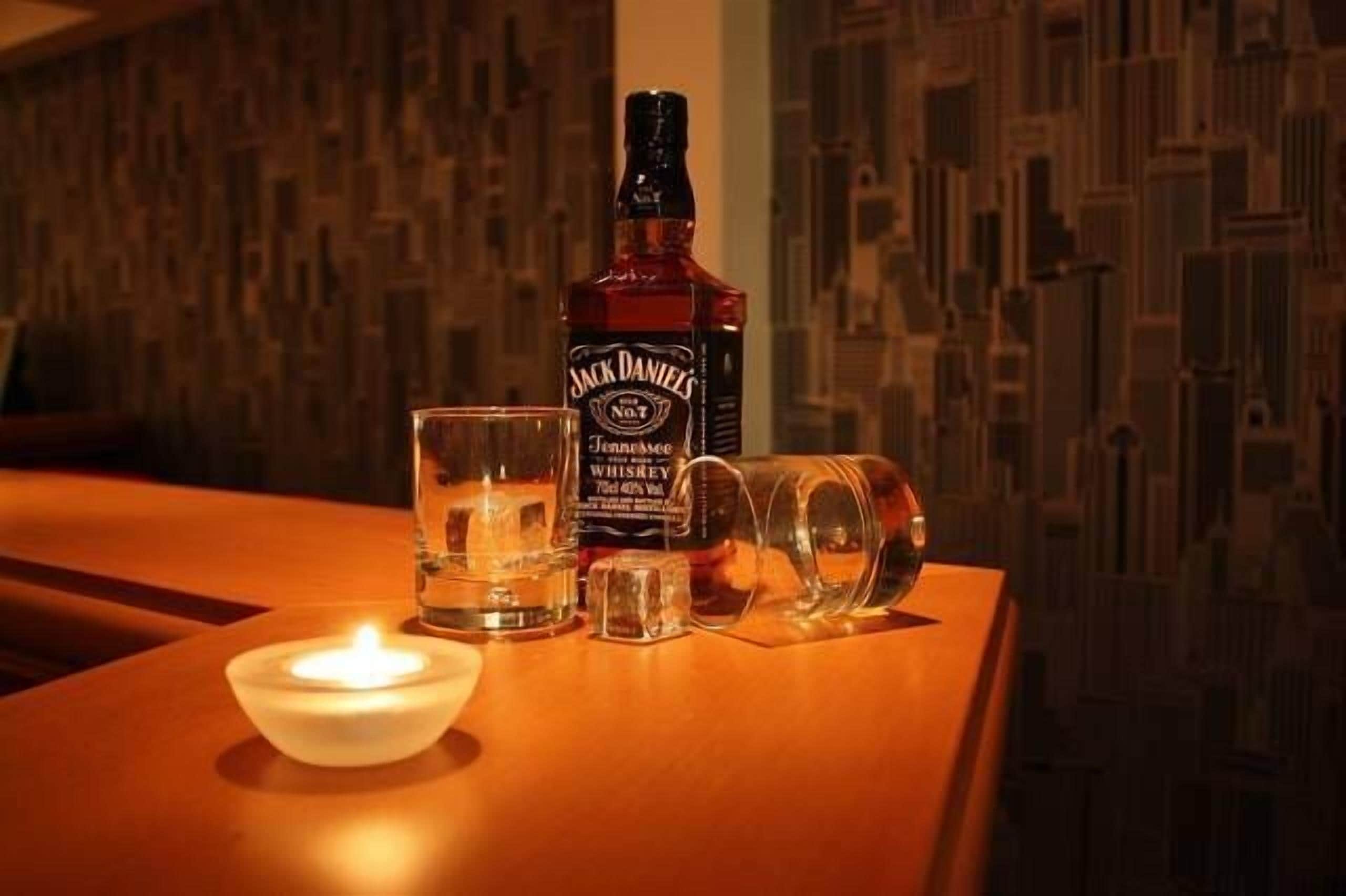 Une bouteille de whisky Jack Daniel's, un verre et une bougie sur une table en bois.