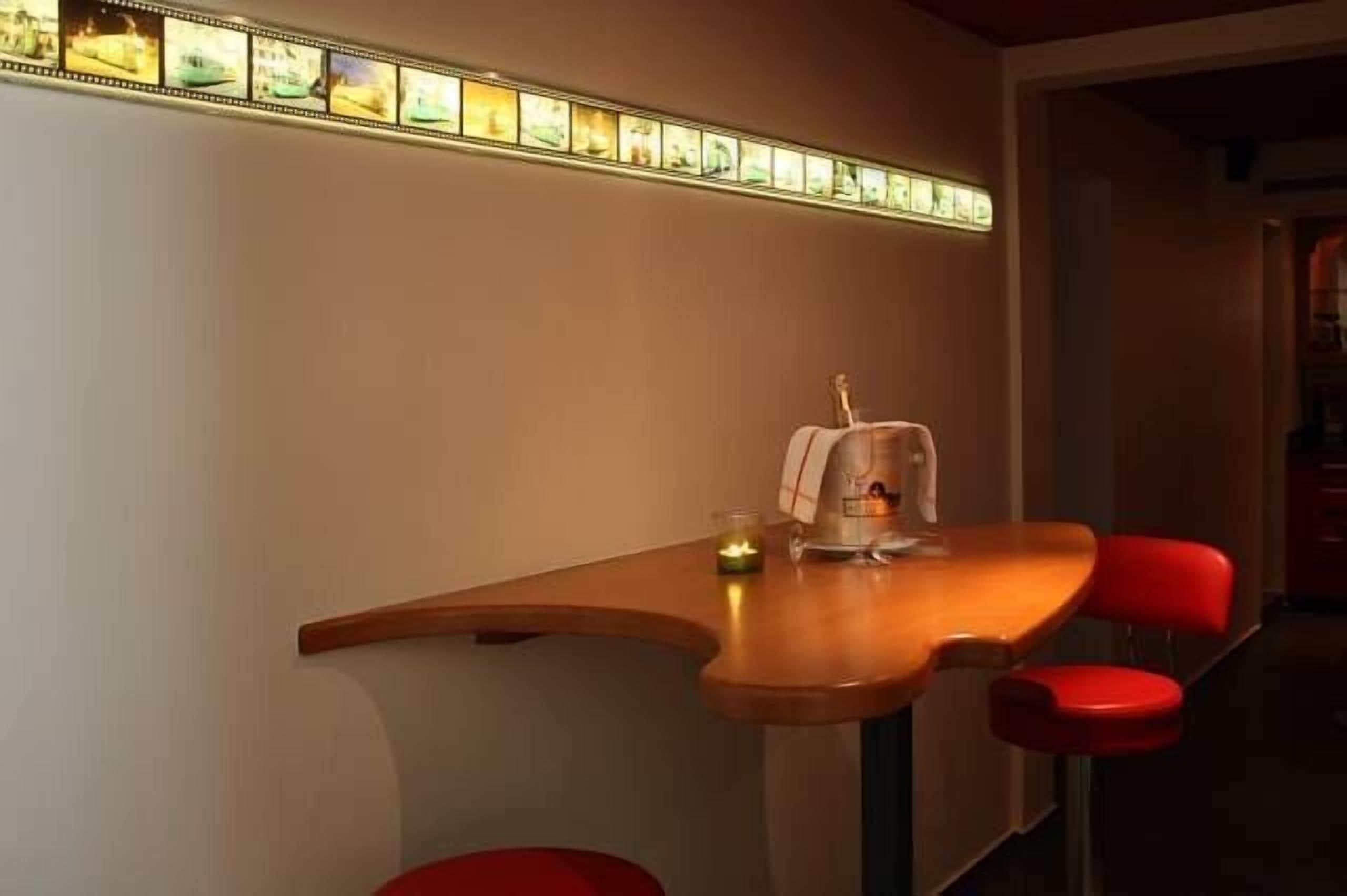 A dining area with a wooden table and red chairs, a candle, and a framed picture on the wall.