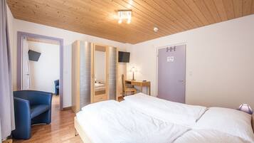 Un dormitorio con una cama grande, un escritorio, una silla y un televisor montado en la pared.