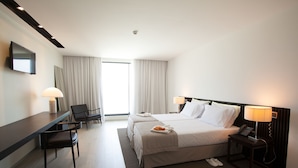 Habitación de hotel con cama, mesitas de noche, escritorio, silla y televisor en la pared.