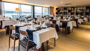 Un restaurante con varias mesas dispuestas para comer, amplios ventanales que ofrecen una vista y una decoración interior moderna.