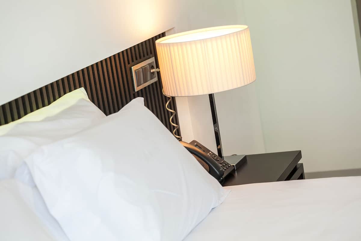 A neatly made bed with white linens and a black nightstand beside it.