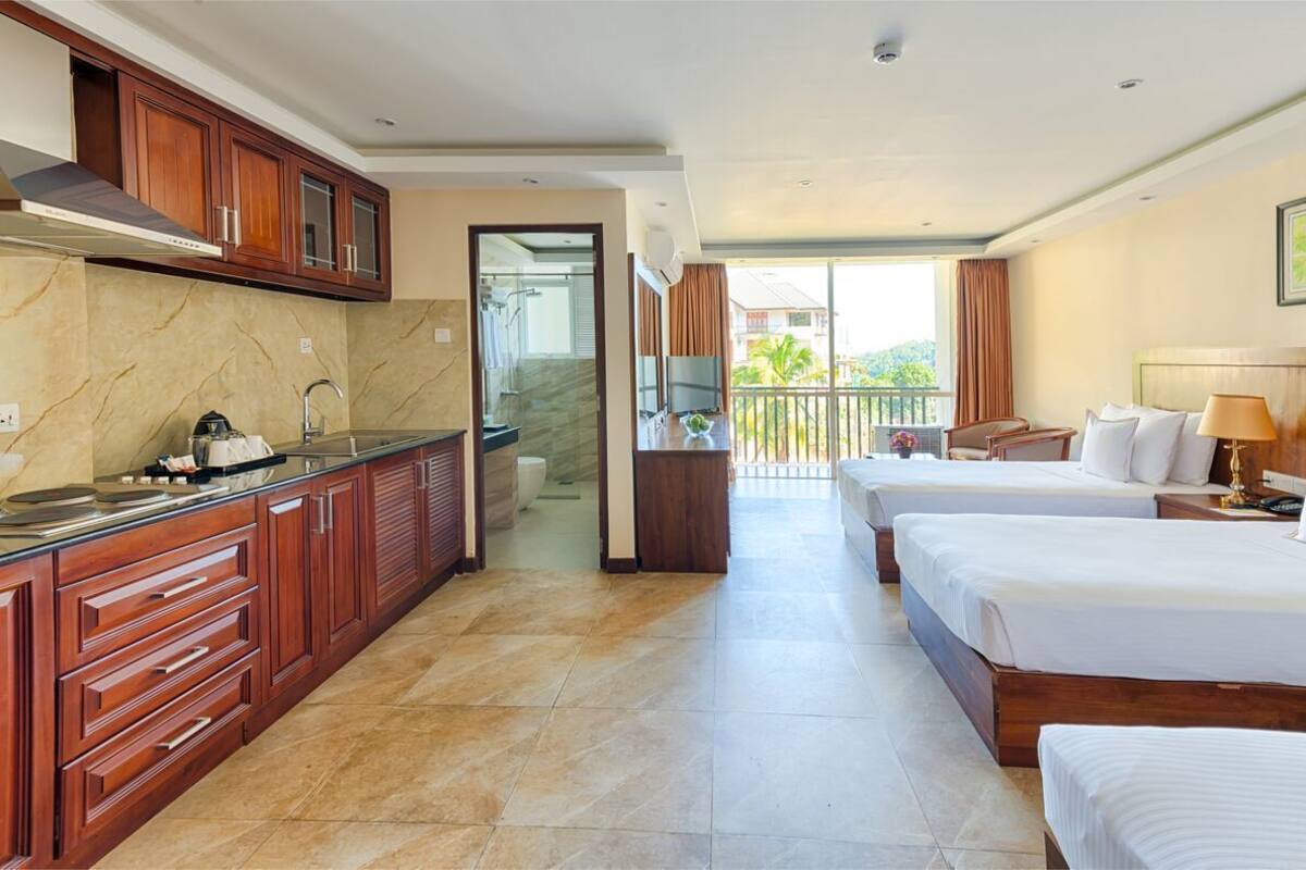 Quarto de hotel com cozinha, duas camas, varanda com vista e chuveiro.