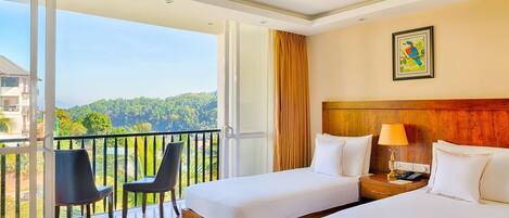 Habitación de hotel con dos camas, un balcón con sillas y vista al bosque.