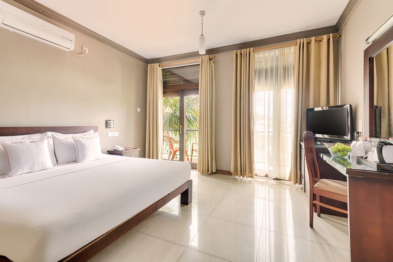 A hotel room with a large bed, a desk with a television, and a view of the outdoors.