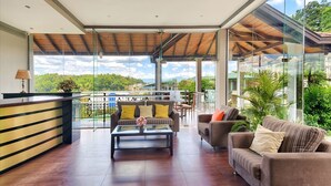 A modern living room with a wooden ceiling, a glass wall, and a view of a lush landscape. - Serene Kandy (Kandy)