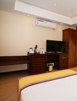 Una habitación de hotel con cama, televisor, escritorio de madera, banco y unidad de aire acondicionado.