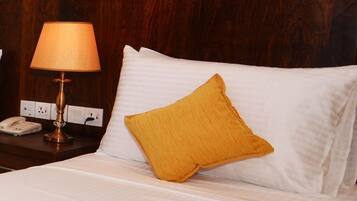 A hotel room with a wooden headboard, a bedside lamp, a telephone, and a bed with white bedding and a yellow pillow.