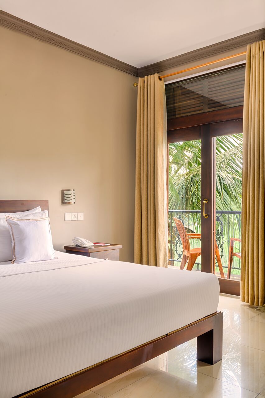 A hotel room with a large bed, a bedside table with a phone, and a view of the outdoors through a sliding glass door.