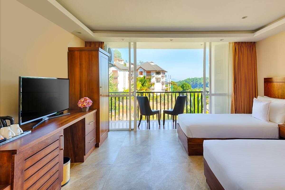 Quarto de hotel com varanda, televisão, secretária com computador, duas camas e uma cadeira.
