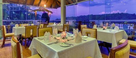 Un restaurante con mesas dispuestas para comer, amplias ventanas que ofrecen vistas al paisaje y una estructura de techo de madera.