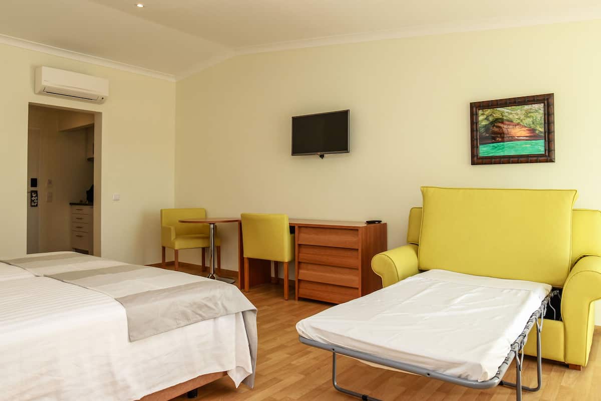 A hotel room with a bed, a desk, two chairs, a TV, and a painting on the wall.