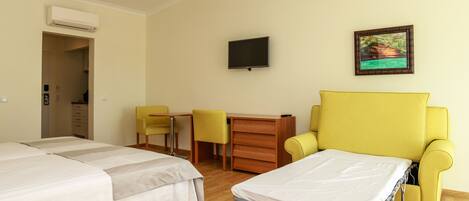 A hotel room with a bed, a desk, two chairs, a TV, and a painting on the wall.
