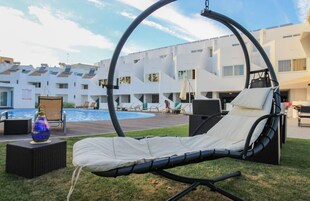 Una silla de lounge circular al aire libre con cojín, una mesita con un objeto decorativo y una piscina al fondo.
