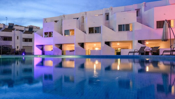 Un hotel moderno con piscina, varios balcones y zonas de estar al aire libre.