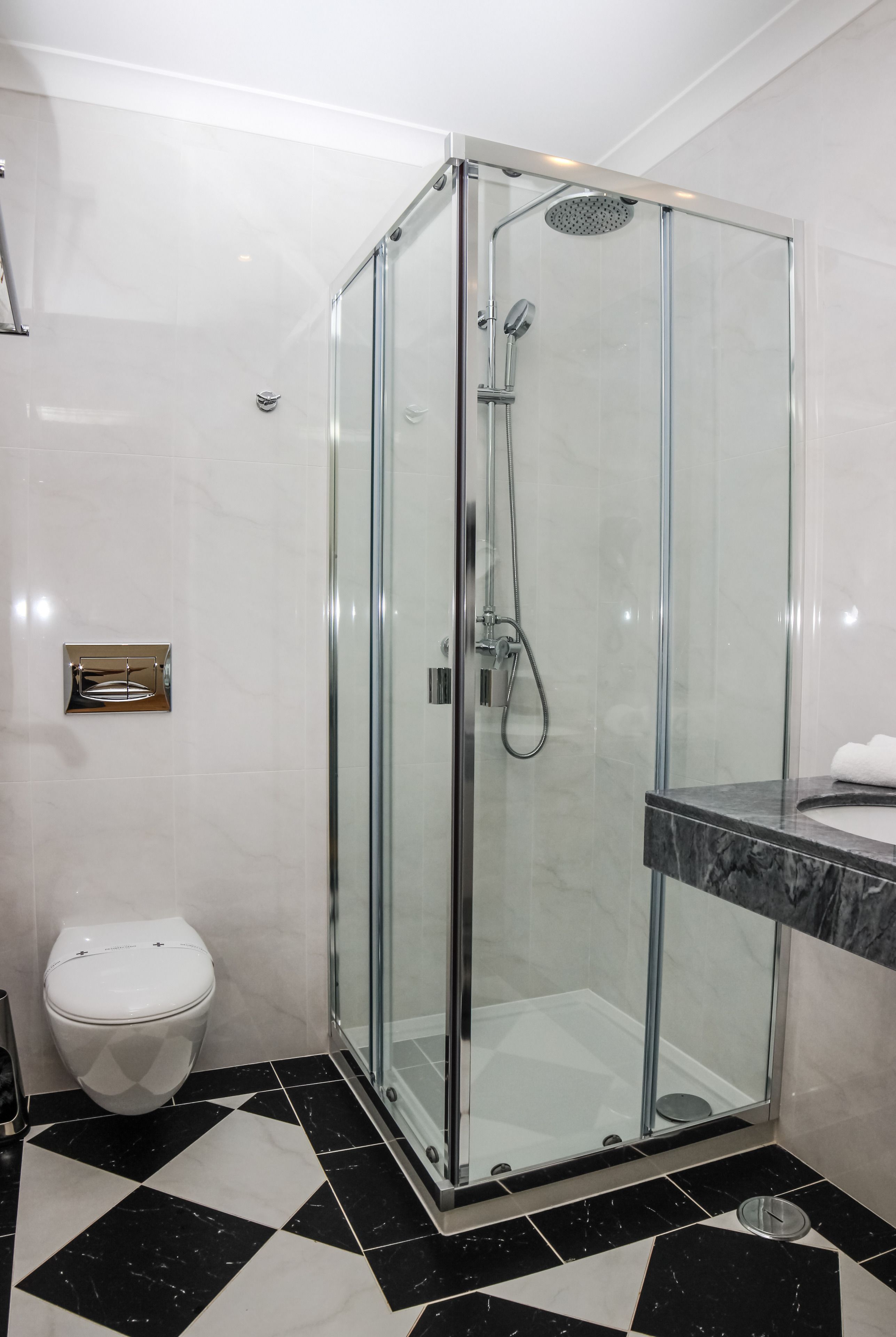 A modern bathroom with a glass-enclosed shower, a white toilet, and a marble-tiled floor.