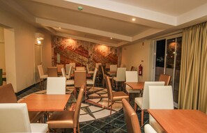 A hotel dining area with multiple tables and chairs, a fire extinguisher, and a large window with curtains. - Lagoa Hotel (Lagoa)
