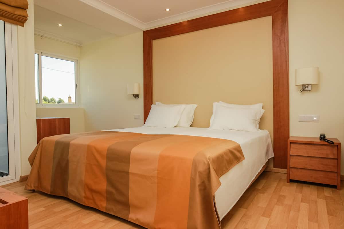 A hotel room with a large bed, wooden headboard, two bedside tables, and a window with a view.