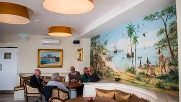 Un vestíbulo con un mural de una escena de playa, una mesa redonda con un florero y un grupo de personas sentadas alrededor de una mesa.