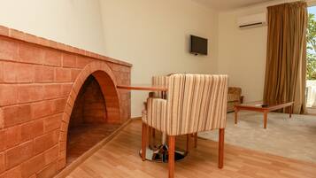 Una habitación con chimenea de ladrillo, un sillón a rayas, una mesa de madera, un televisor y una ventana con cortinas.