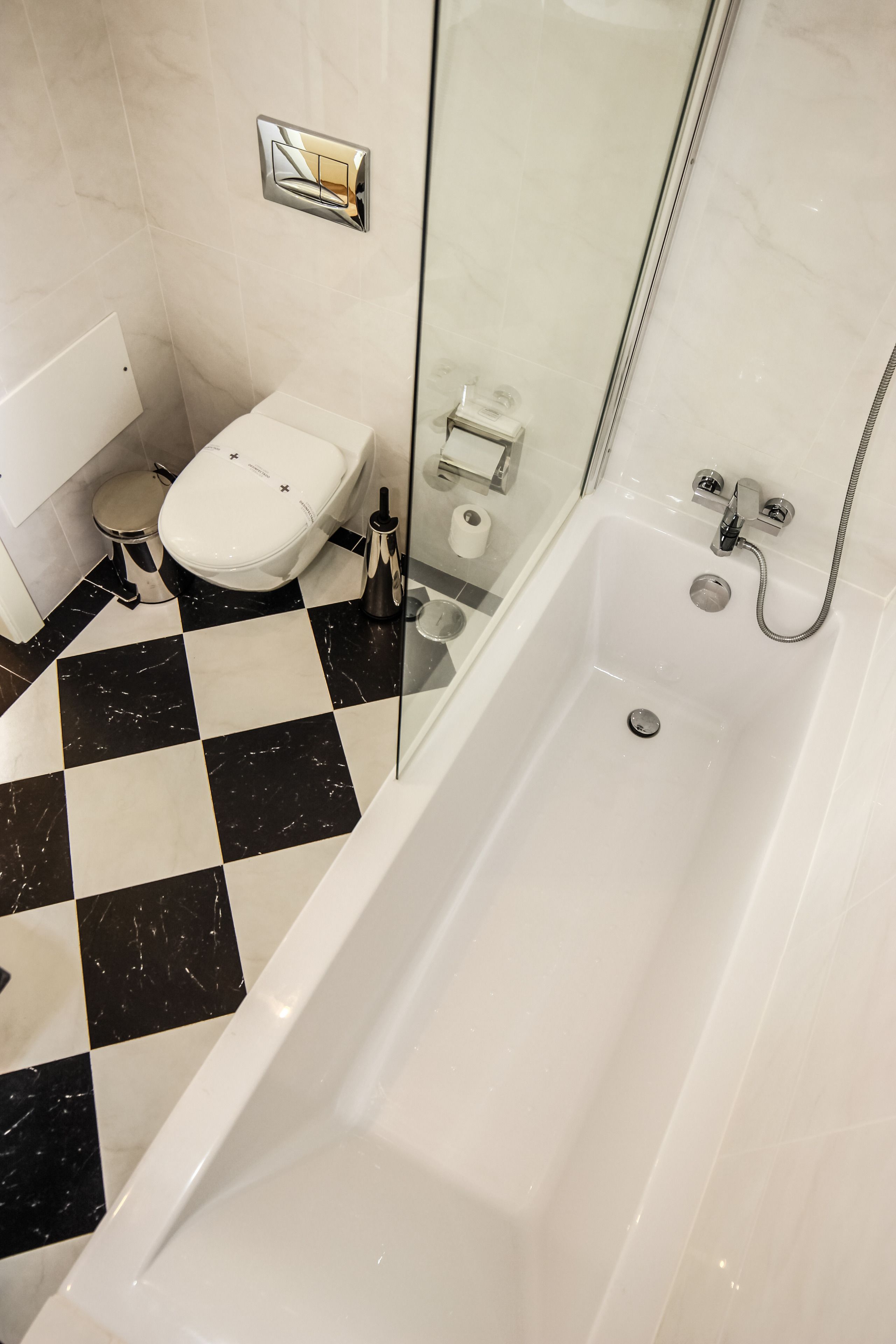 Een badkamer met een zwart-wit betegelde vloer, een witte badkuip, een toilet en een douchecabine met glazen wanden.