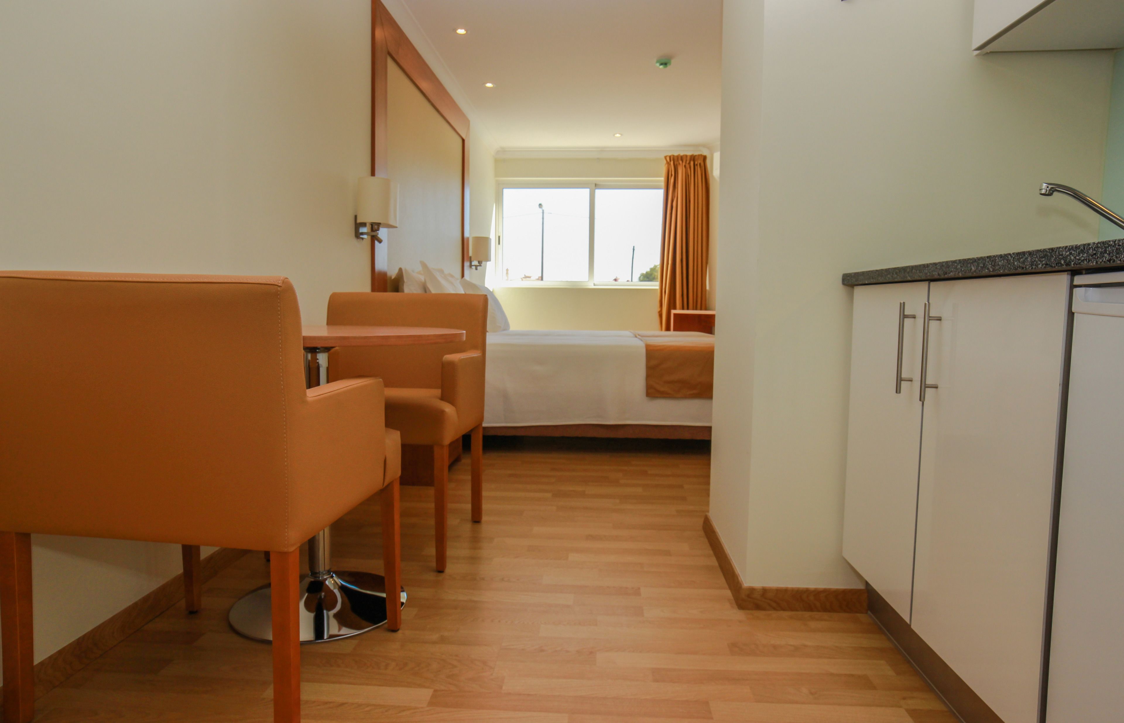 A hotel room with a bed, a small table with chairs, a kitchenette, and a window with curtains.