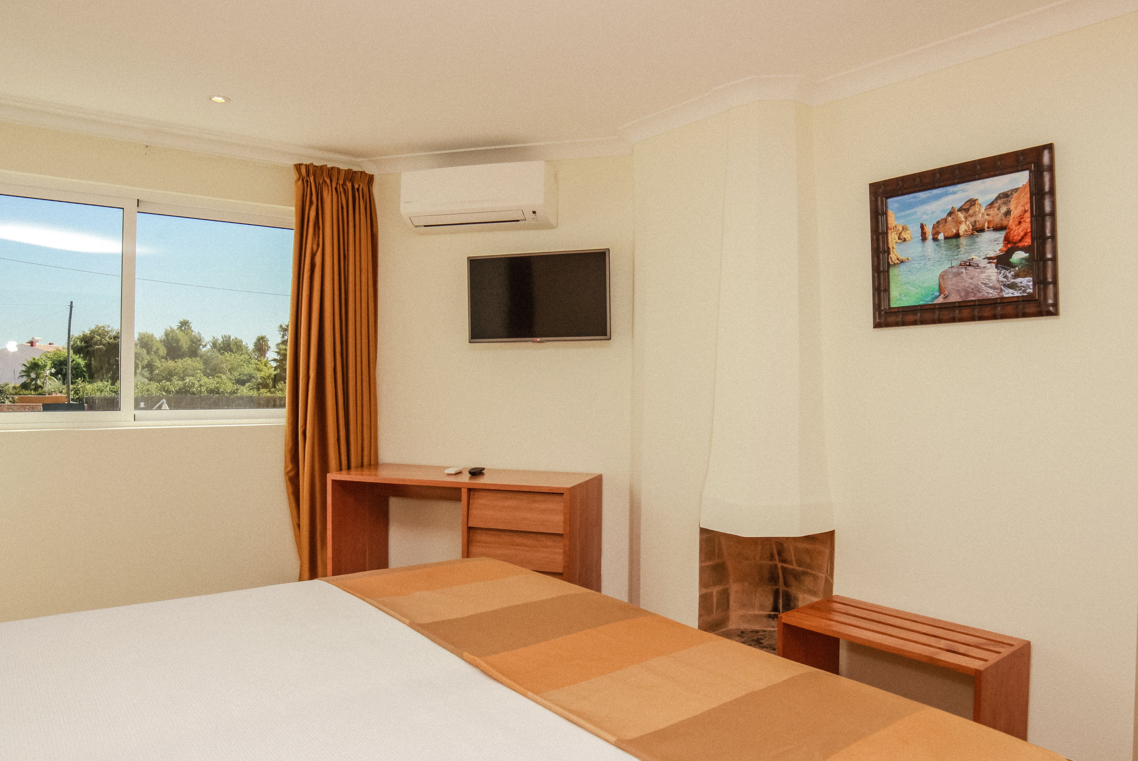Una habitación de hotel con cama, escritorio, televisor y un cuadro en la pared.