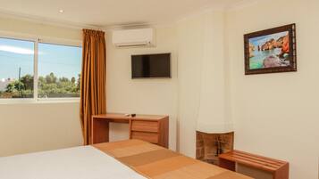 Una habitación de hotel con cama, escritorio, televisor y un cuadro en la pared.