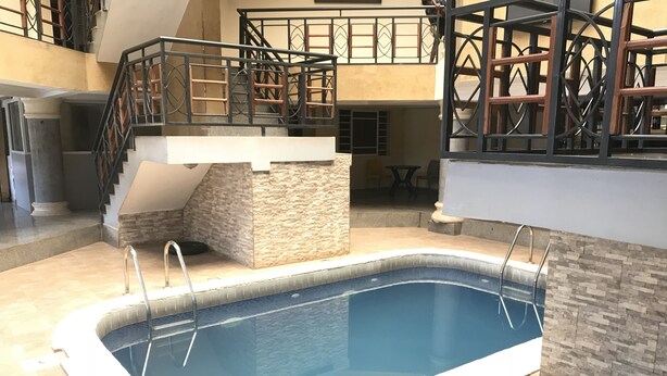 An indoor swimming pool with a stone accent wall, a staircase, and a balcony with a railing. - Pentagon Luxury Suites Enugu (Enugu)