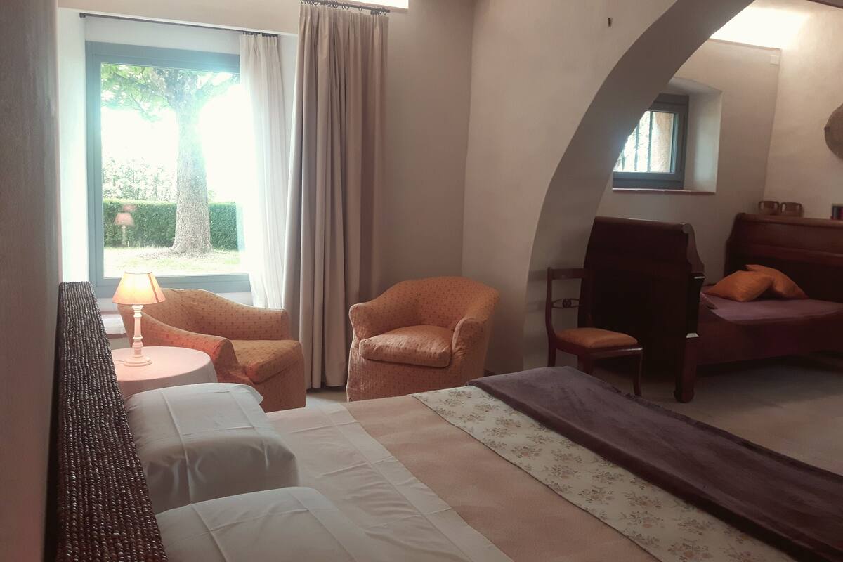 A hotel room with a bed, two armchairs, a small table with a lamp, and a window with curtains.
