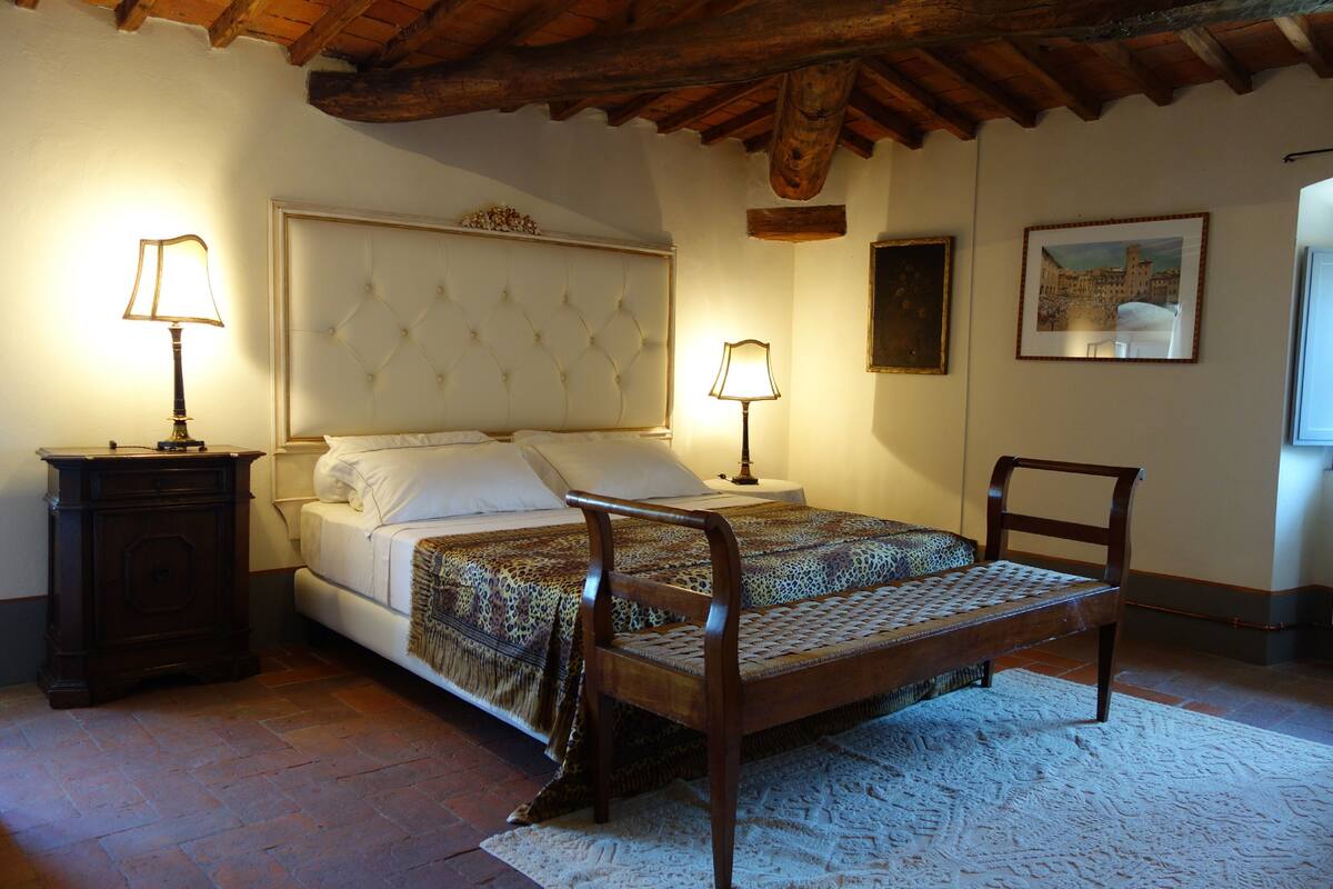 A bedroom with a large bed, two bedside tables with lamps, a wooden bench, and a framed picture on the wall.