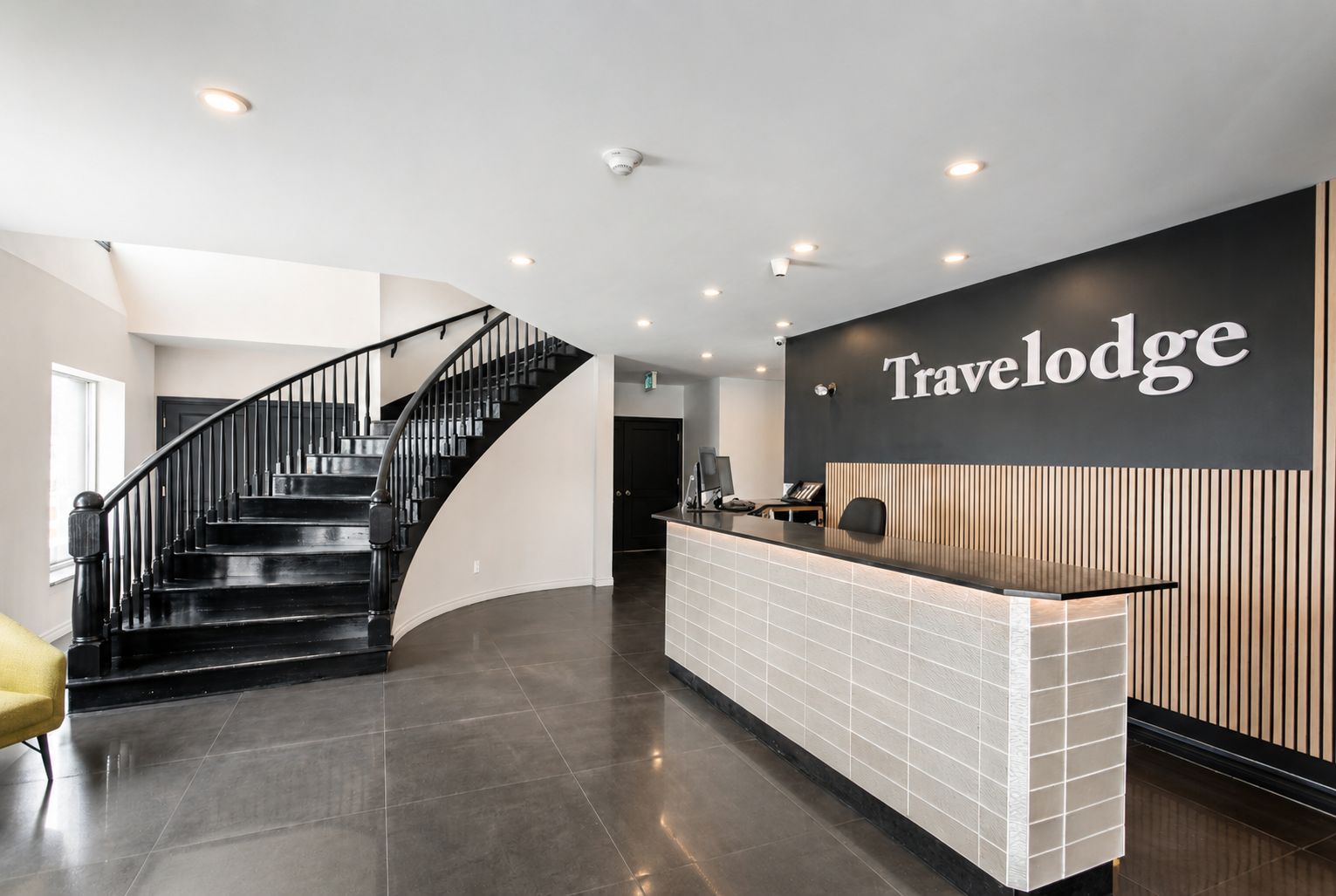 Una zona de recepción con una escalera curva, un mostrador de recepción y un cartel en la pared que dice 'Travelodge'.