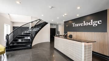 Una zona de recepción con una escalera curva, un mostrador de recepción y un cartel en la pared que dice 'Travelodge'.