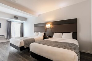 A hotel room with two beds, a large window with curtains, a wall-mounted light fixture, and a wooden floor.