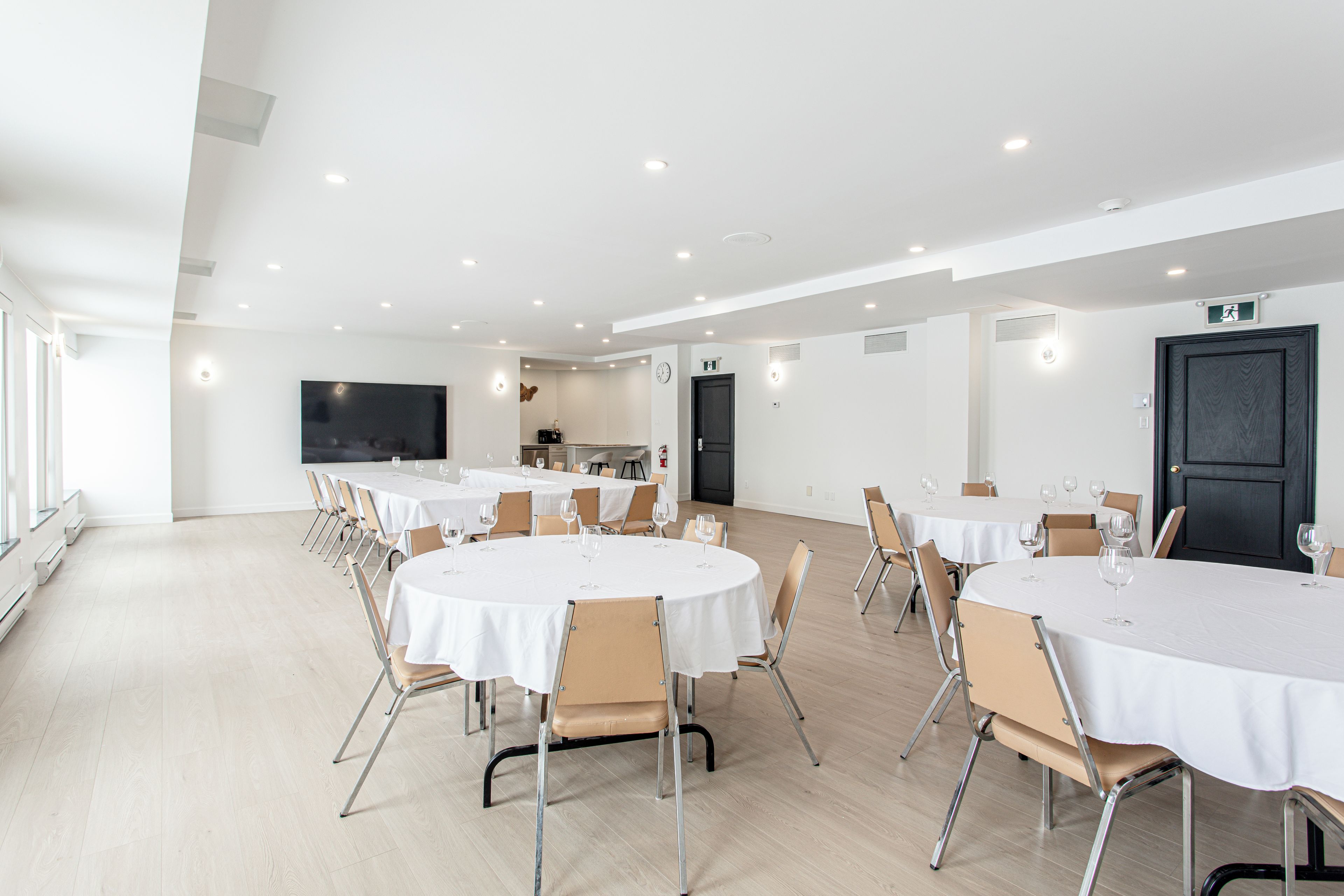 A spacious conference room with multiple round tables, each set with chairs and wine glasses.