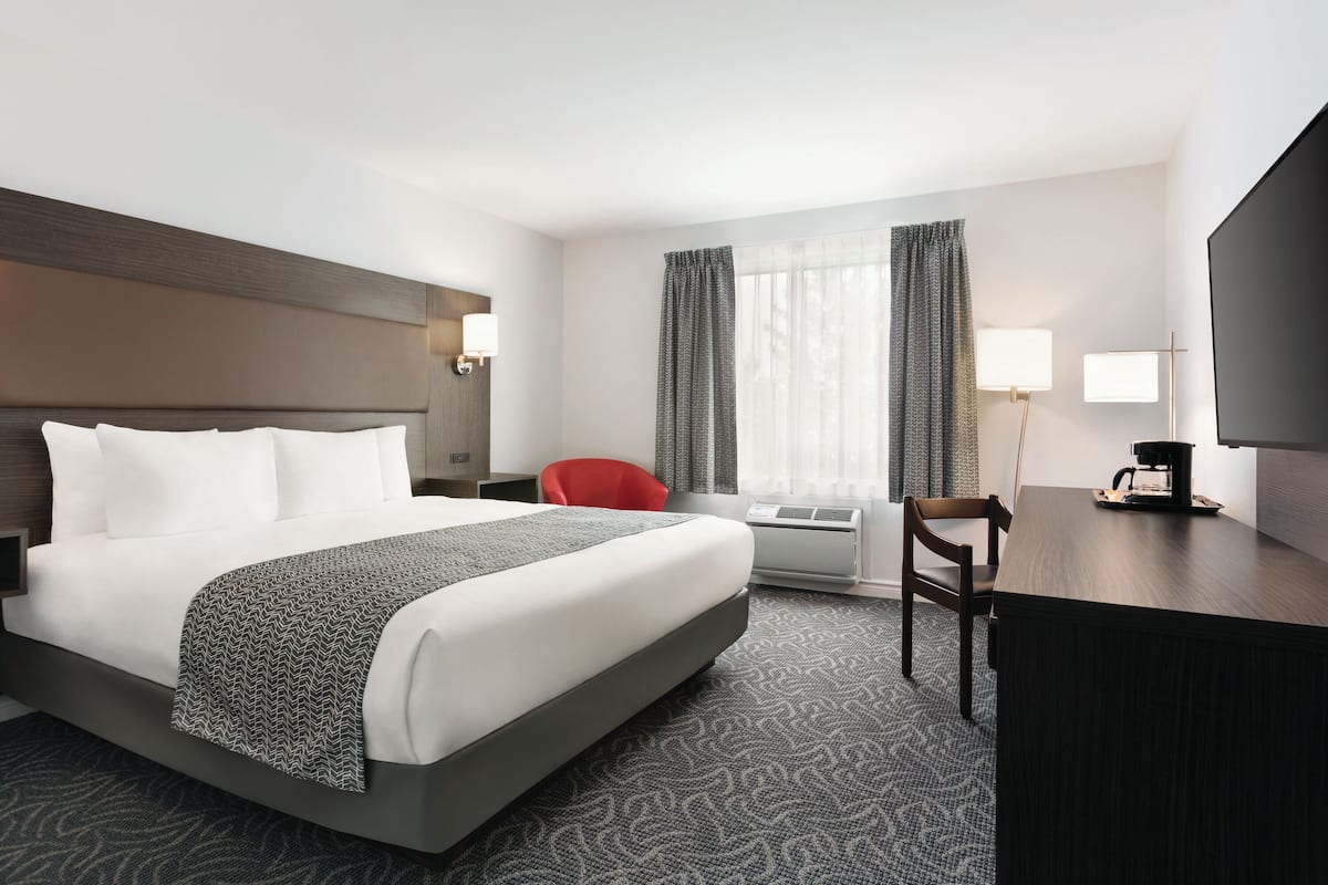 A hotel room with a large bed, a desk, a chair, an air conditioning unit, and a television.