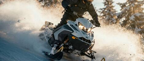 A snowmobile in motion, kicking up snow, with a forested background.