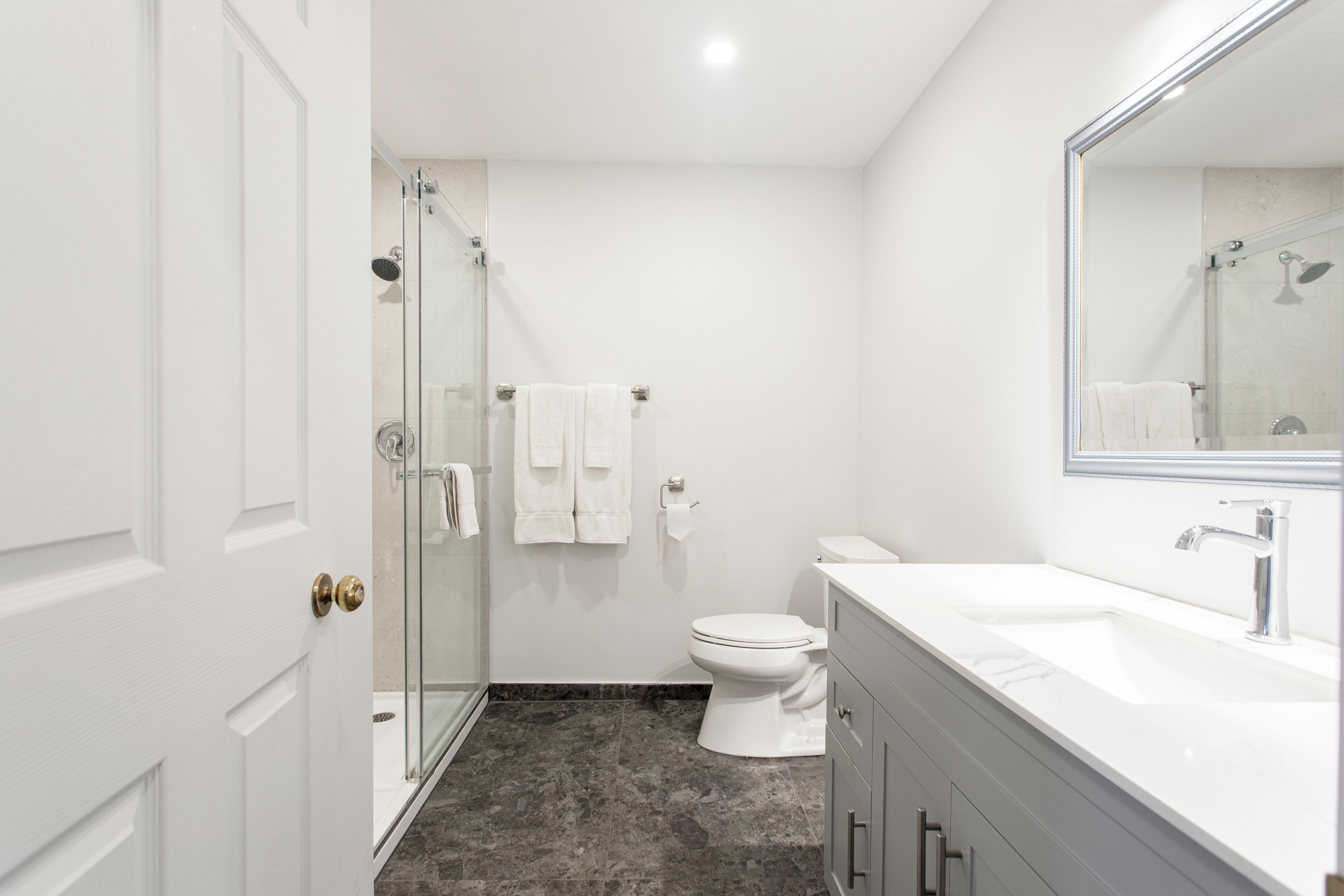 Un baño moderno con cabina de ducha de vidrio, inodoro blanco y tocador con espejo.