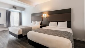 Habitación de hotel con dos camas, un ventanal con cortinas, una lámpara fijada a la pared y suelo de madera.