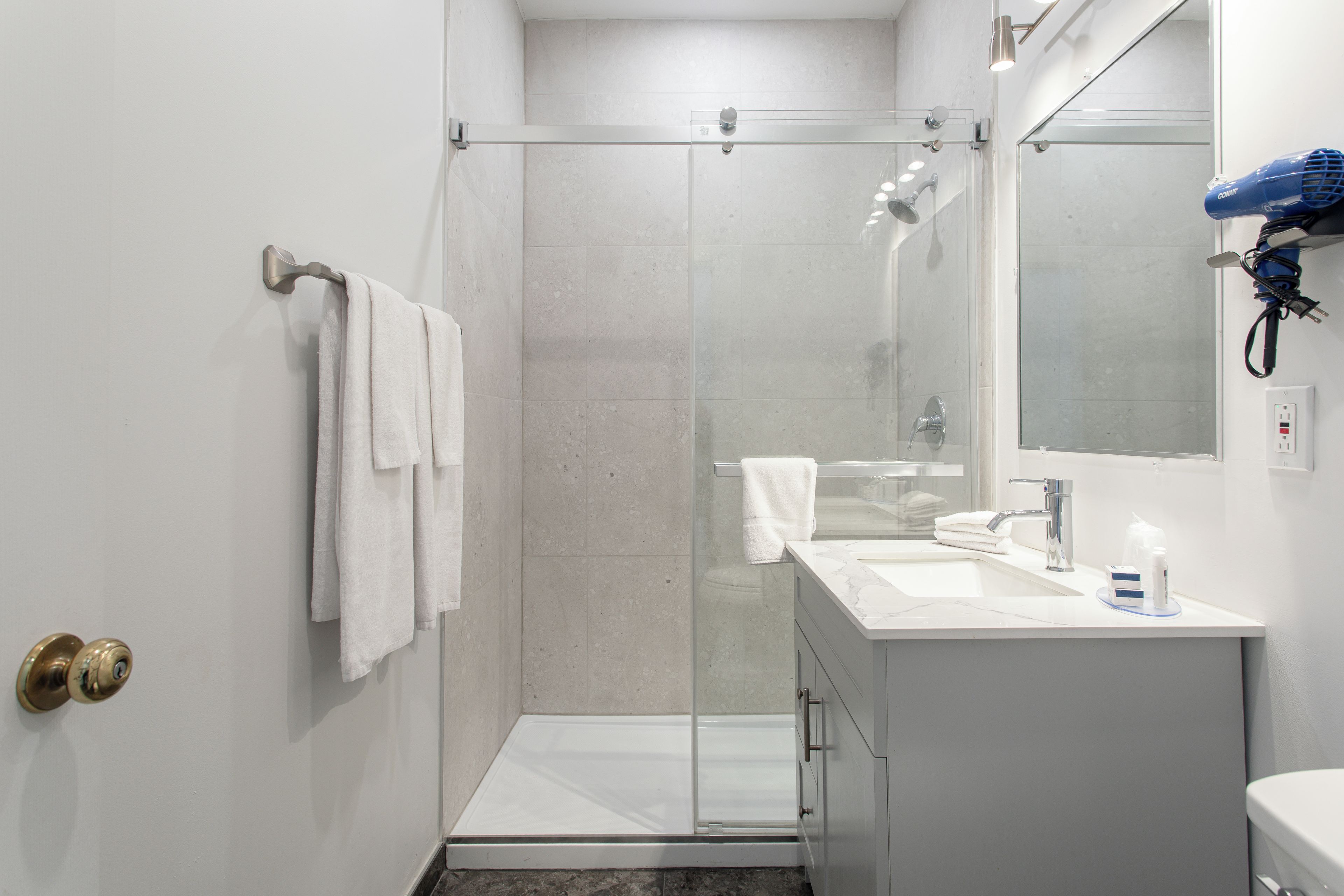 Un baño moderno con cabina de ducha de vidrio, un lavamanos blanco y un espejo sobre el lavabo.