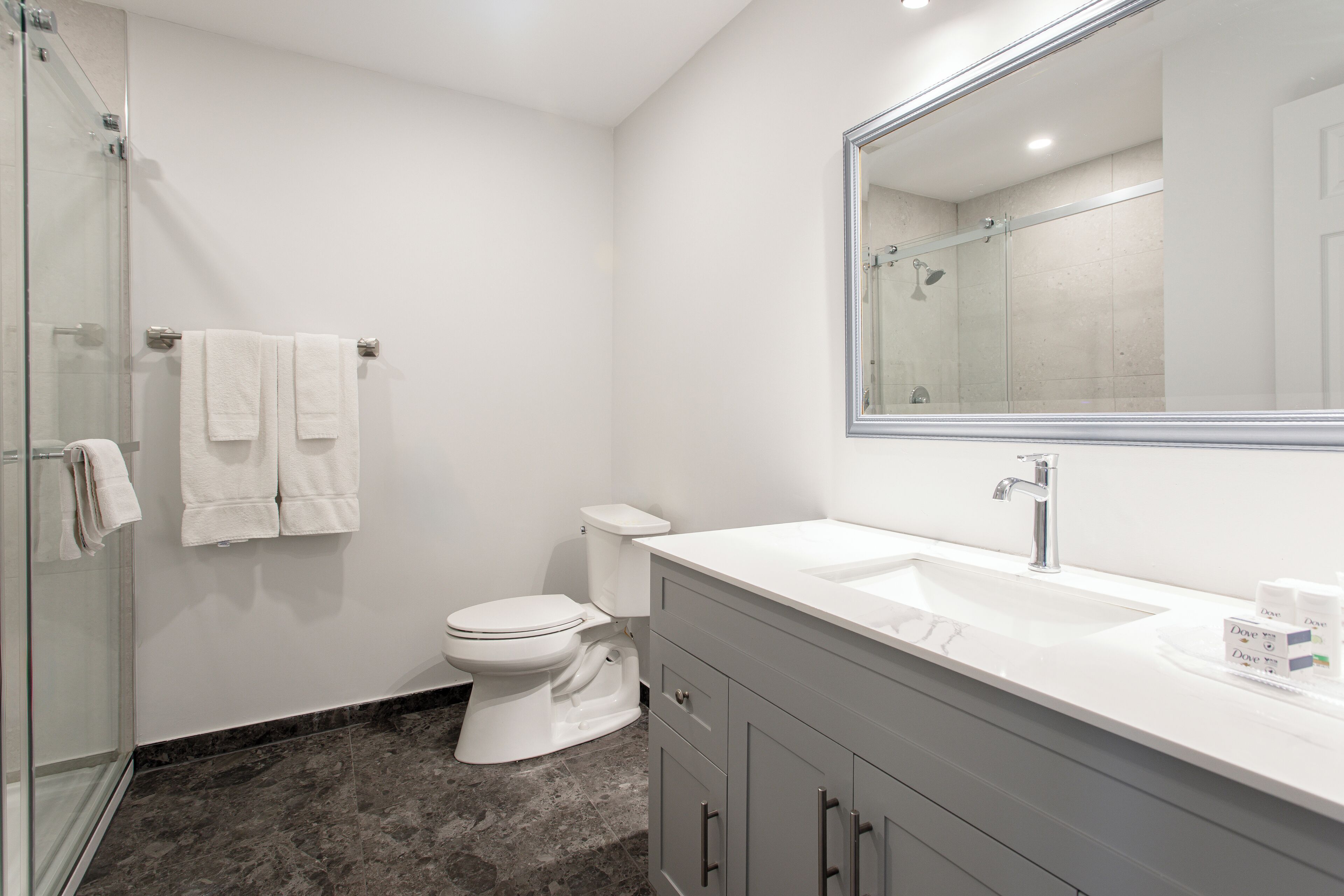 Un baño moderno con cabina de ducha de vidrio, inodoro blanco y tocador con espejo grande.