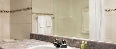 A bathroom with a white sink, a shower, and a marble countertop.