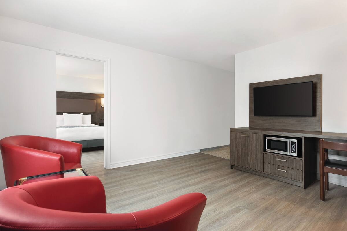 A hotel room with a bed, a TV, a microwave, and red chairs.